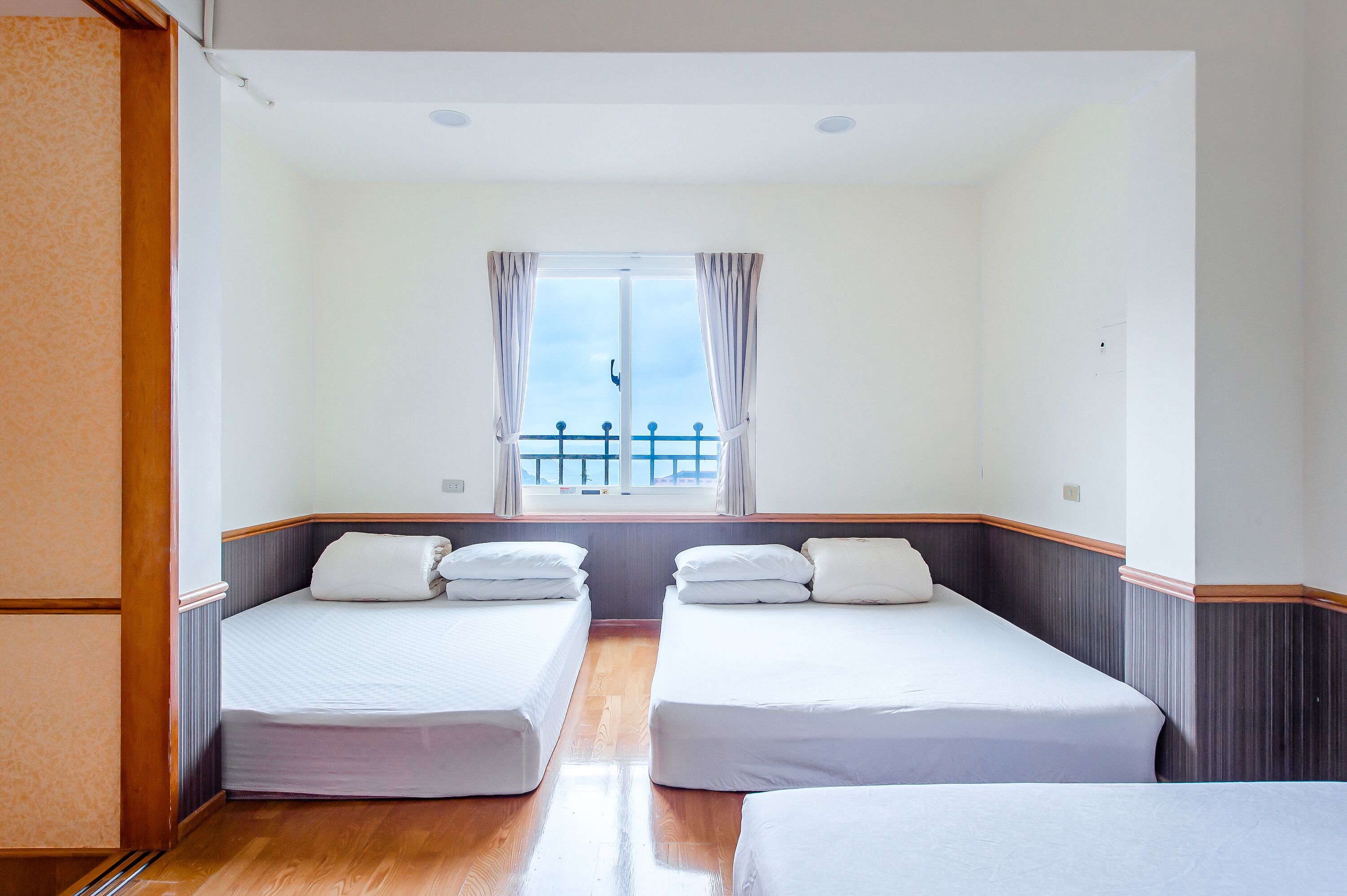 Habitación de hotel con dos camas individuales, una ventana con cortinas y vista a un balcón.