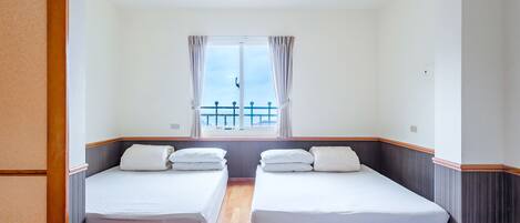 Habitación de hotel con dos camas individuales, una ventana con cortinas y vista a un balcón.
