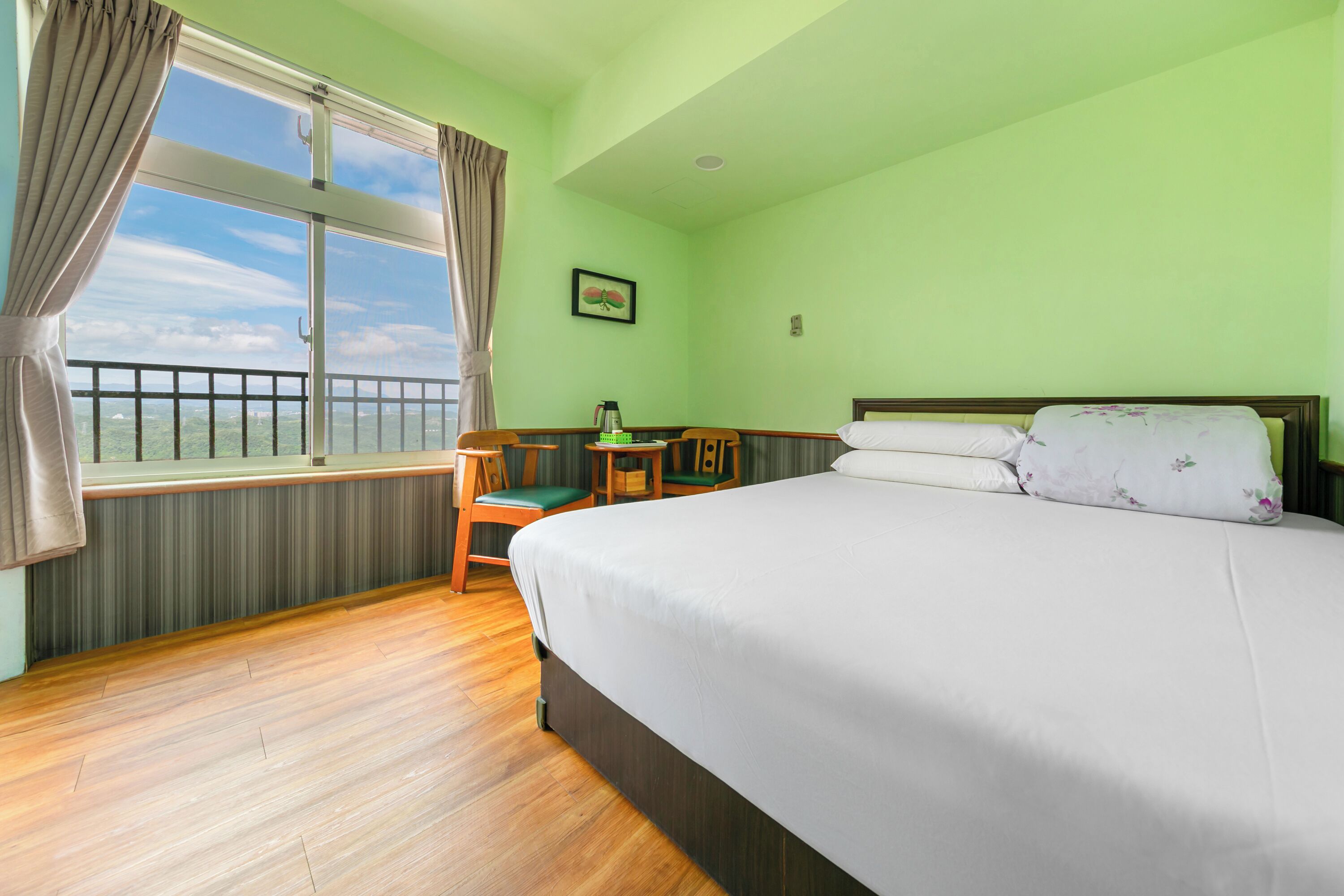 A hotel room with a large bed, a small desk with a chair, a window with curtains, and a view of the outside.