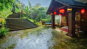 A traditional wooden building with a sloped roof and red lanterns, surrounded by lush greenery and a wet stone staircase. - CF Kite Homestay (New Taipei City)