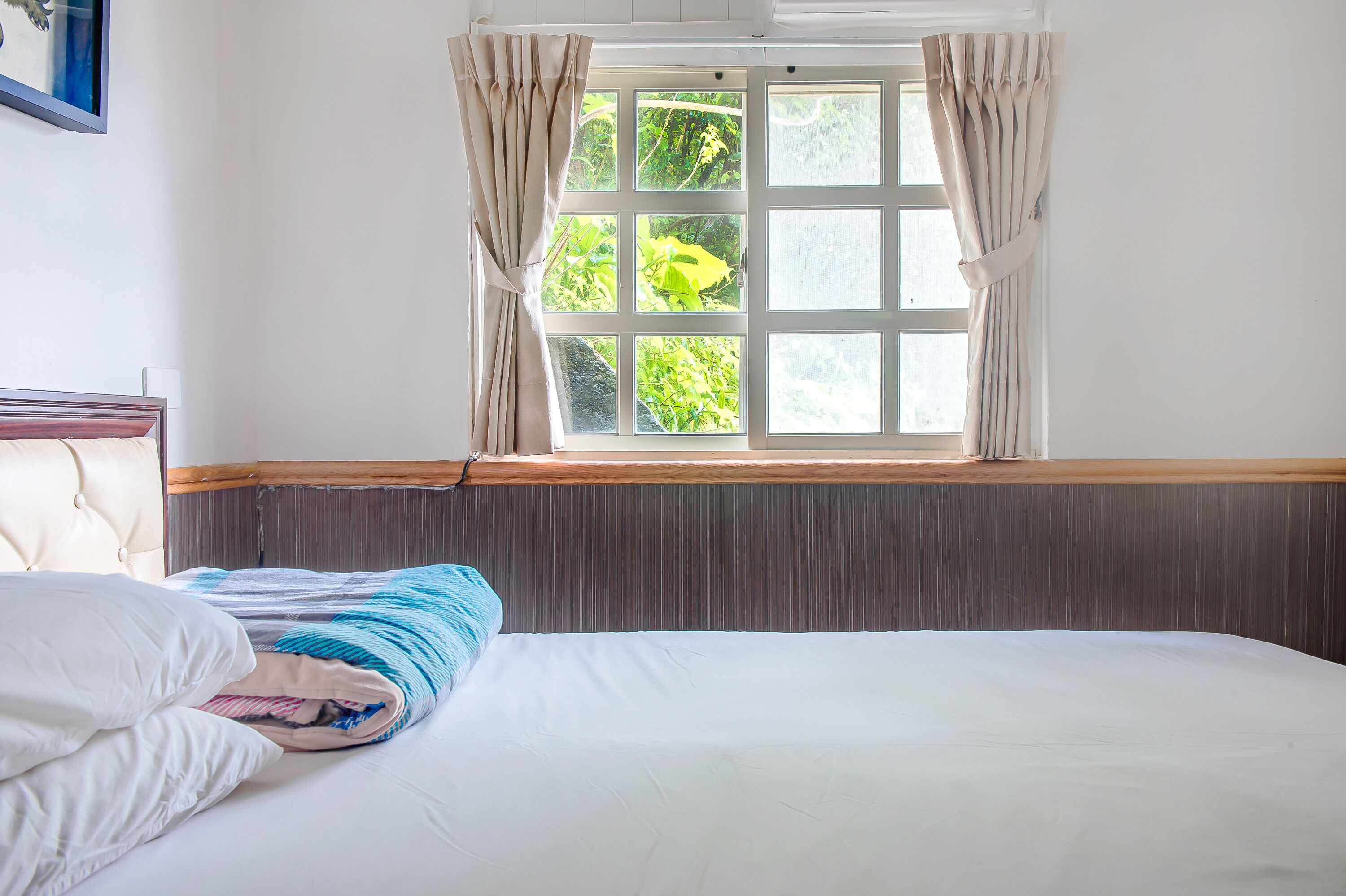 A neatly made bed with a white and blue striped blanket, a wooden headboard, and a window with curtains.