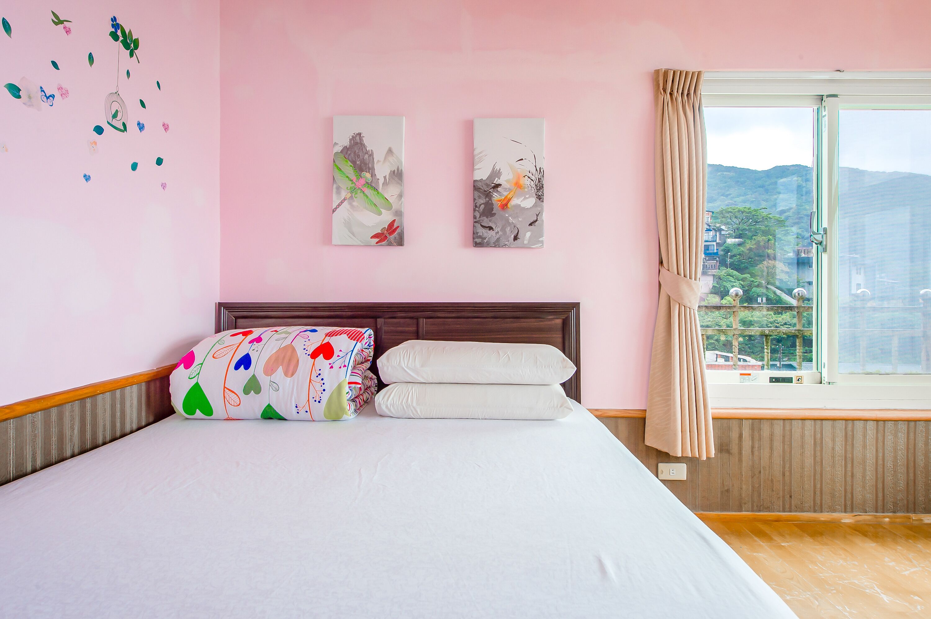 A bedroom with a bed, pillows, a headboard, two wall art pieces, and a window with a view of a cityscape.