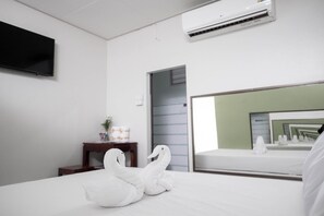 Habitació d'hotel amb llit, televisió de pantalla plana, aire condicionat, una taula de nit amb un ram i un mirall que reflecteix l'habitació.