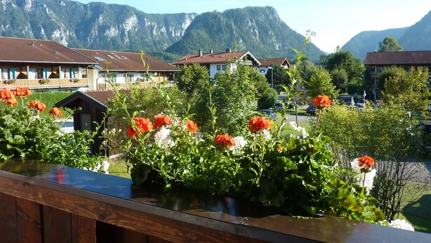 Un pueblo de montaña con casas tradicionales, una terraza de madera con flores y una vista despejada de las montañas.