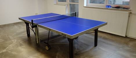 A table tennis table with wheels, positioned in a room with tiled flooring and a window.