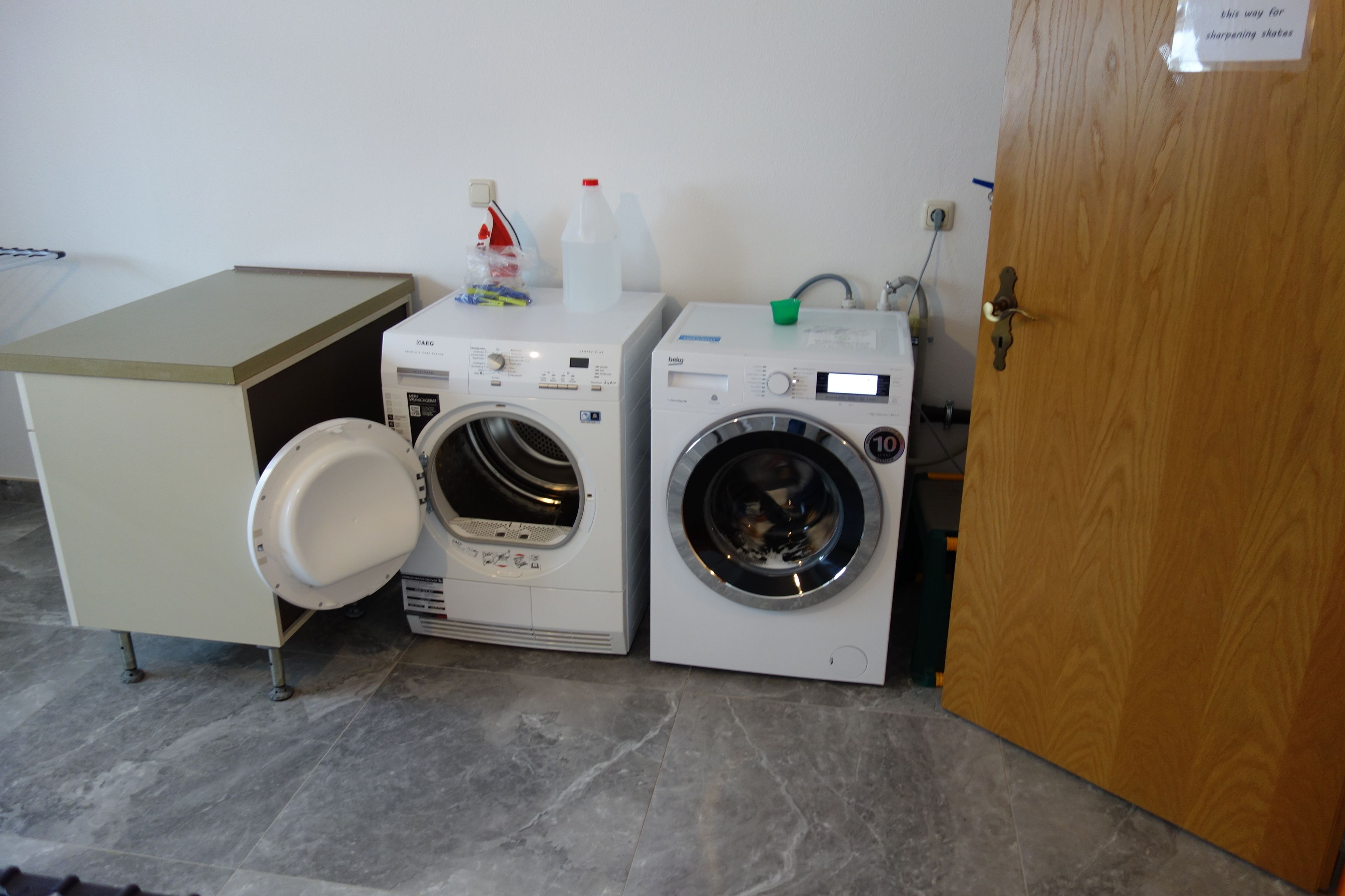Een wasruimte met twee wasmachines, een kast en een houten deur.