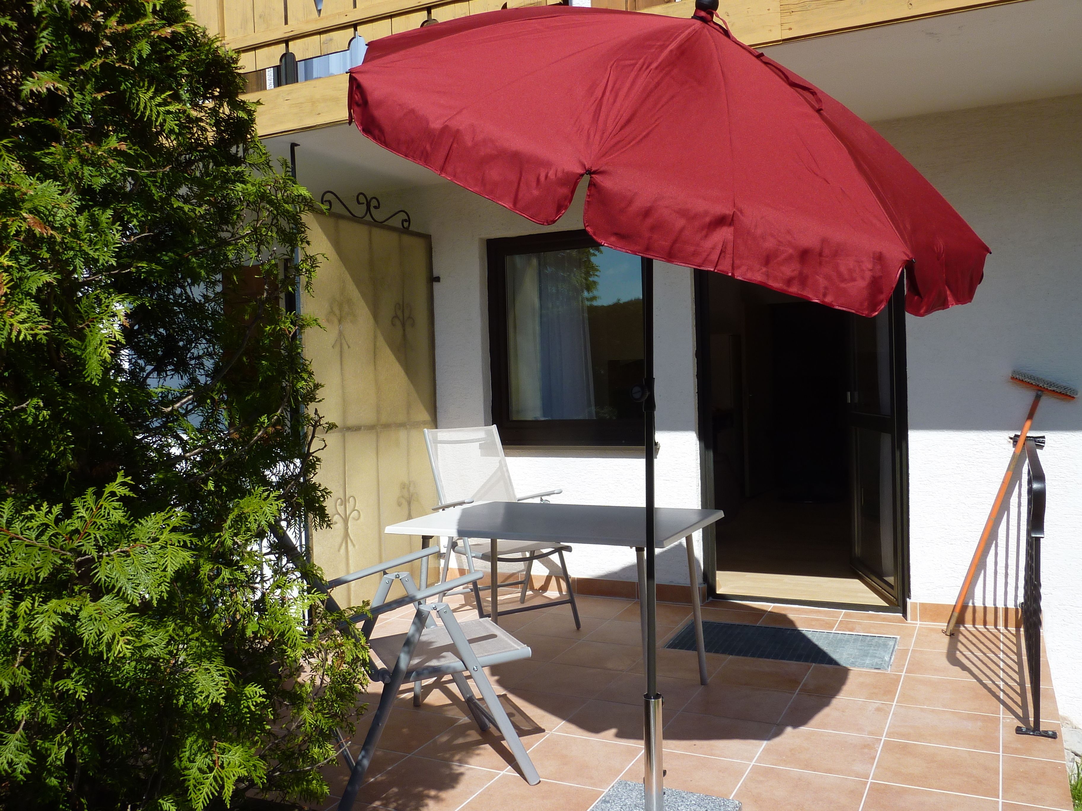A patio with a red umbrella, a white table, and a chair.