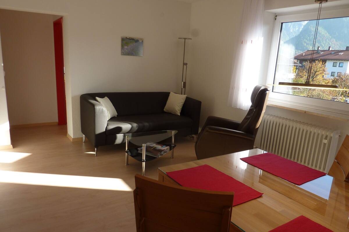 Una sala moderna con un sofá de cuero negro, una mesa de comedor de madera con individuales rojos, un sillón de cuero marrón y un radiador.
