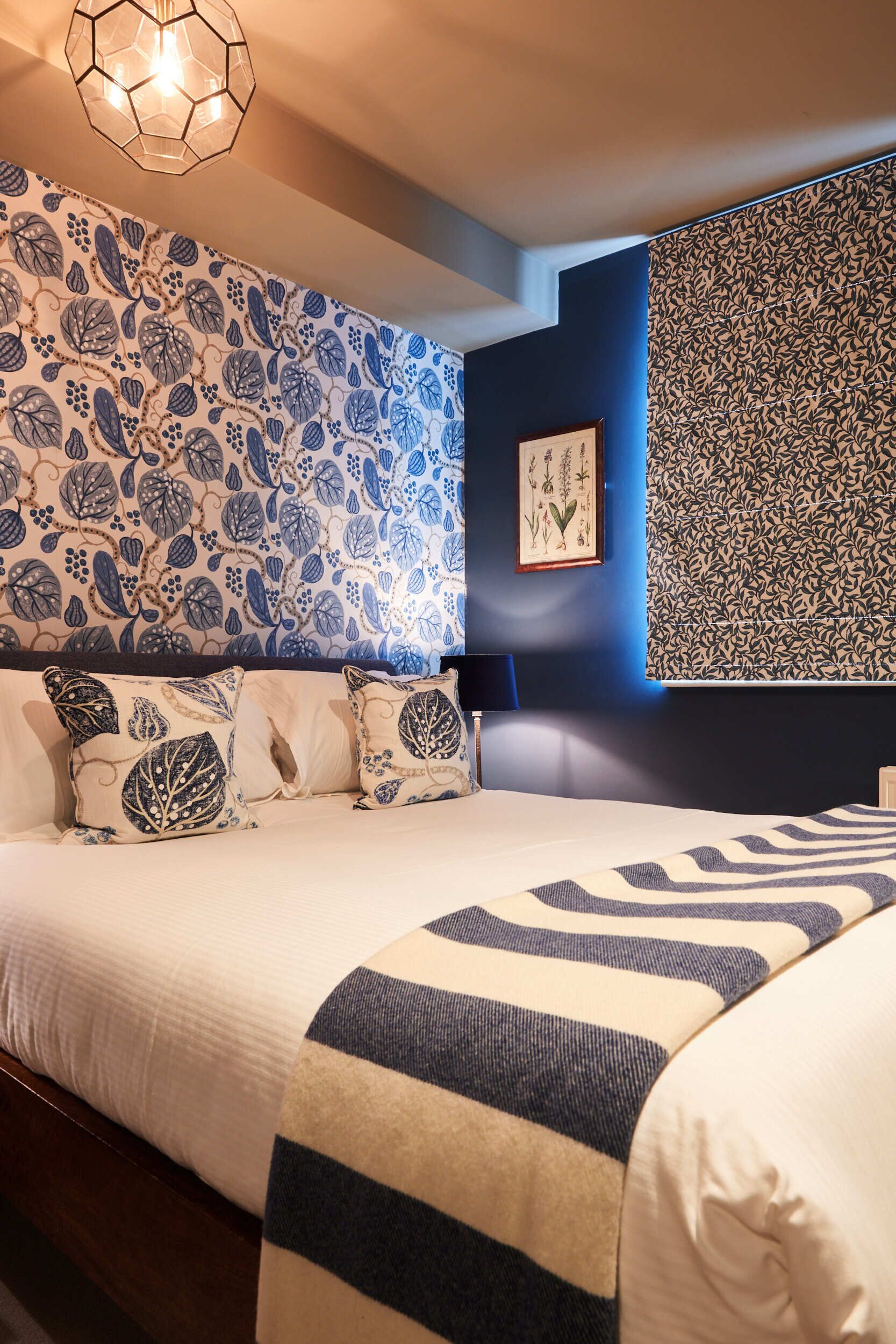 Une chambre à coucher avec un lit, des oreillers et un mur orné d’un motif de feuilles.