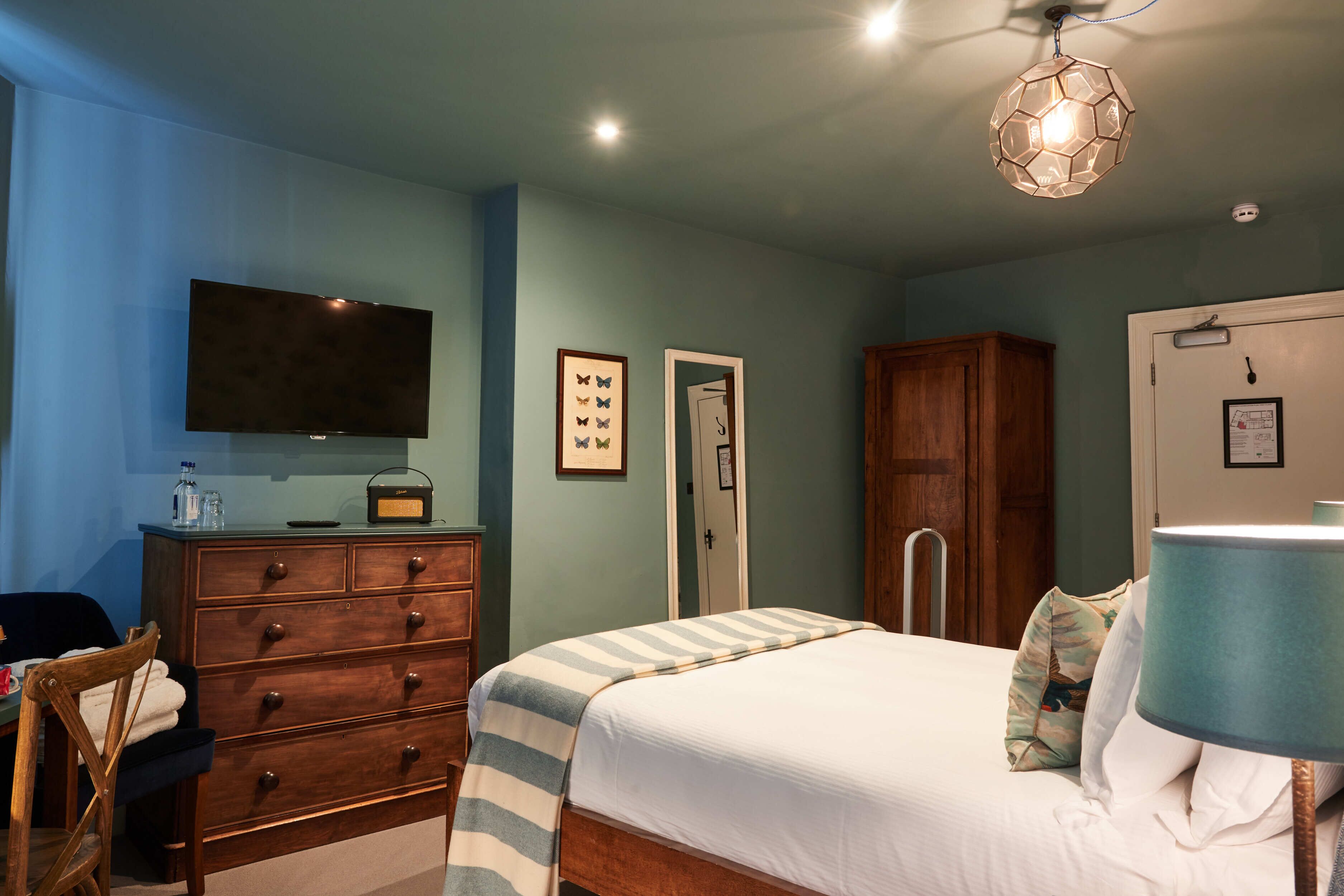 Une chambre à coucher comprenant un lit, une commode, un téléviseur et un luminaire fixé au plafond.