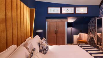 A bedroom with a large bed, wooden headboard, and a wardrobe. There are framed pictures on the wall and a chair in the corner.