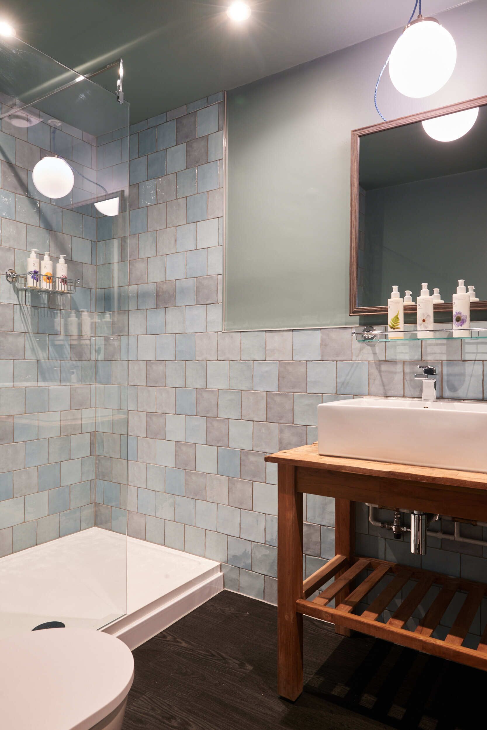 A modern bathroom with a glass shower enclosure, a wooden vanity, and a large mirror.