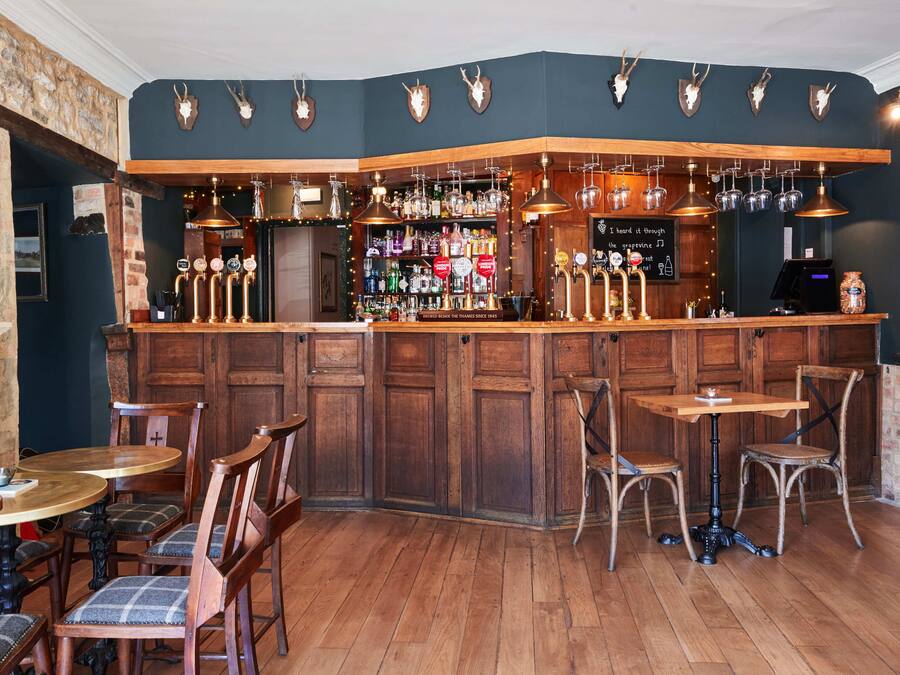 A bar area with wooden furniture, a counter with taps, and shelves with bottles.