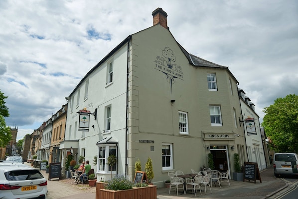 A building with a sign reading "The King's Arms" on the facade, outdoor seating area with chairs and tables, and a parked car in front. - Kings Arms Hotel (Woodstock)