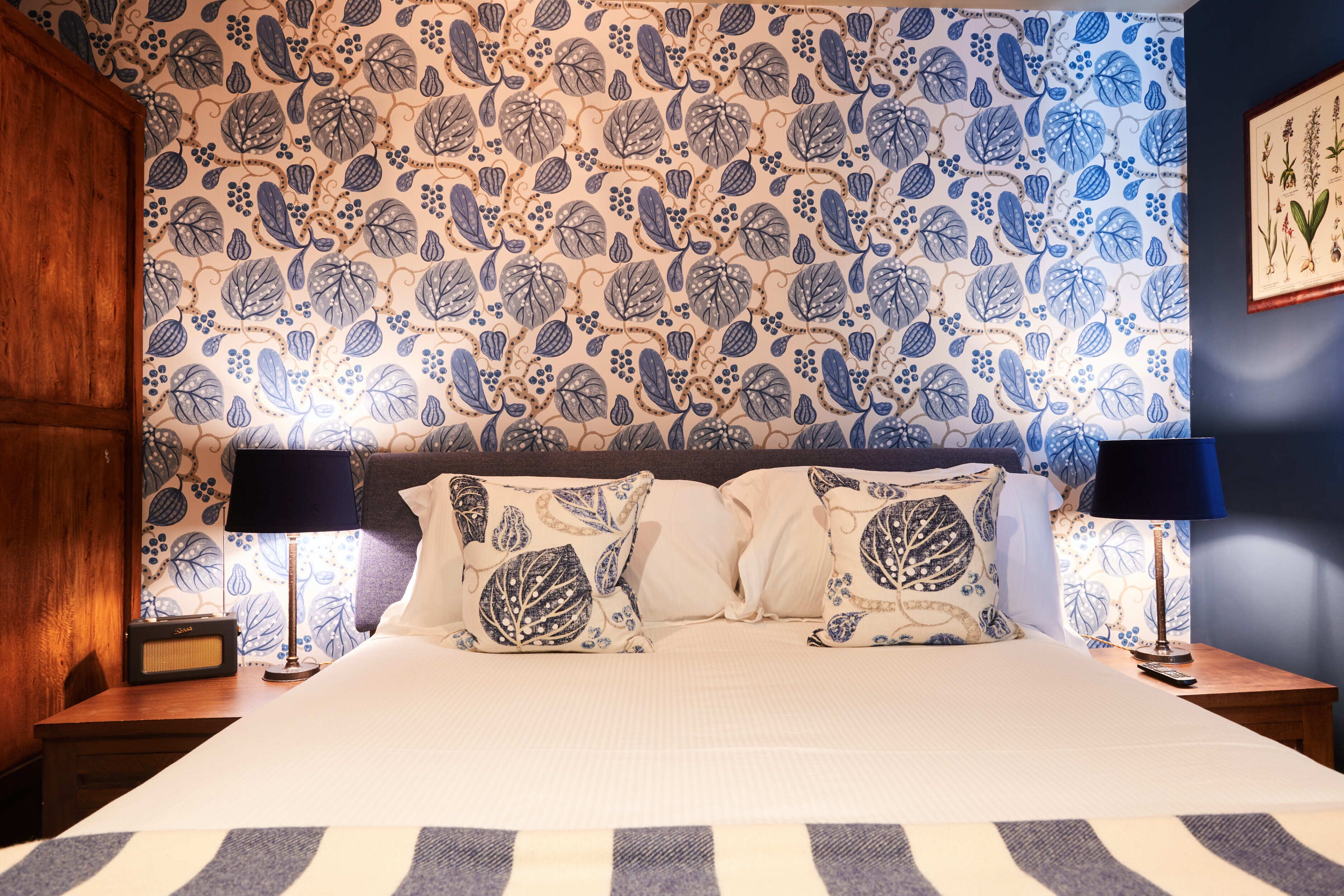 A neatly made bed with patterned pillows, a radio, and a lamp on a wooden nightstand.