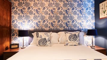A neatly made bed with patterned pillows, a radio, and a lamp on a wooden nightstand.