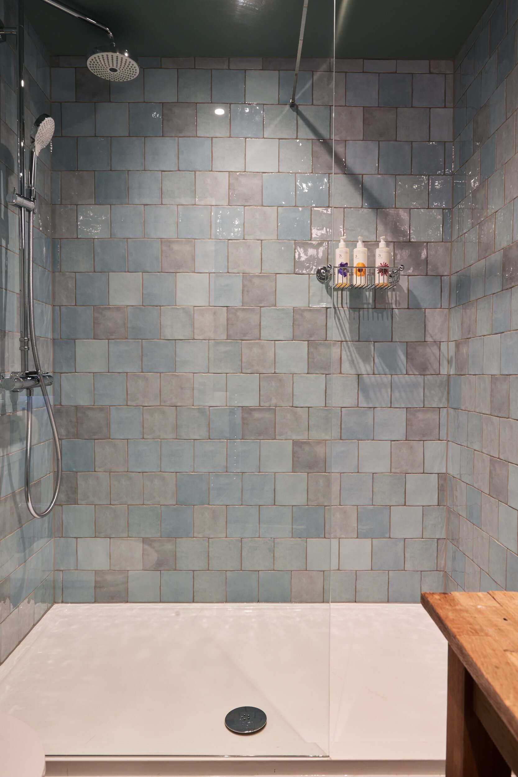 A shower area with a tiled wall, a handheld showerhead, and a glass-enclosed shower stall.