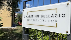 Un letrero que dice 'Charming Bellagio Boutique Hotel & Spa', con una vista clara de la entrada y follaje circundante.