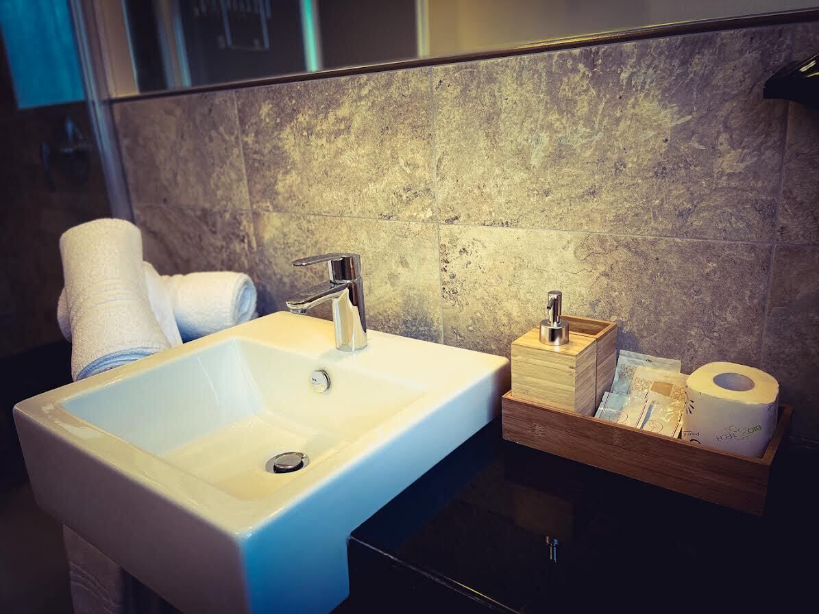 Une salle de bain avec un lavabo blanc, un robinet moderne et une boîte en bois contenant des articles de toilette.