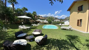 Un patio trasero con piscina, sillas de descanso y un área de comedor con mobiliario de mimbre.