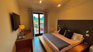 Habitación de hotel con cama, mesita de noche, lámpara y vistas al exterior a través de un ventanal.