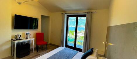 A hotel room with a bed, a desk, a chair, a TV, and a balcony with a view.