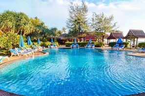 A swimming pool with lounge chairs and umbrellas, surrounded by greenery and buildings. - Prukrom Guesthouse (Ko Lanta)