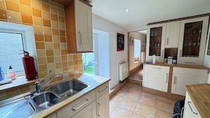 A kitchen with a double sink, wooden cabinets, a fire extinguisher, and a view to the outside. - Charming Beachside Cottage, just had cancelation ,avail now 22-31st Aug,7 d min (Shaldon)