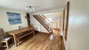 Una habitación amplia con suelo de madera, una mesa de comedor con sillas, una escalera y un cuadro en la pared.