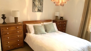 A neatly arranged bedroom with a wooden bed, two bedside tables with lamps, a wall-mounted painting, and a chandelier. - Charming Beachside Cottage, just had cancelation ,avail now 22-31st Aug,7 d min (Shaldon)