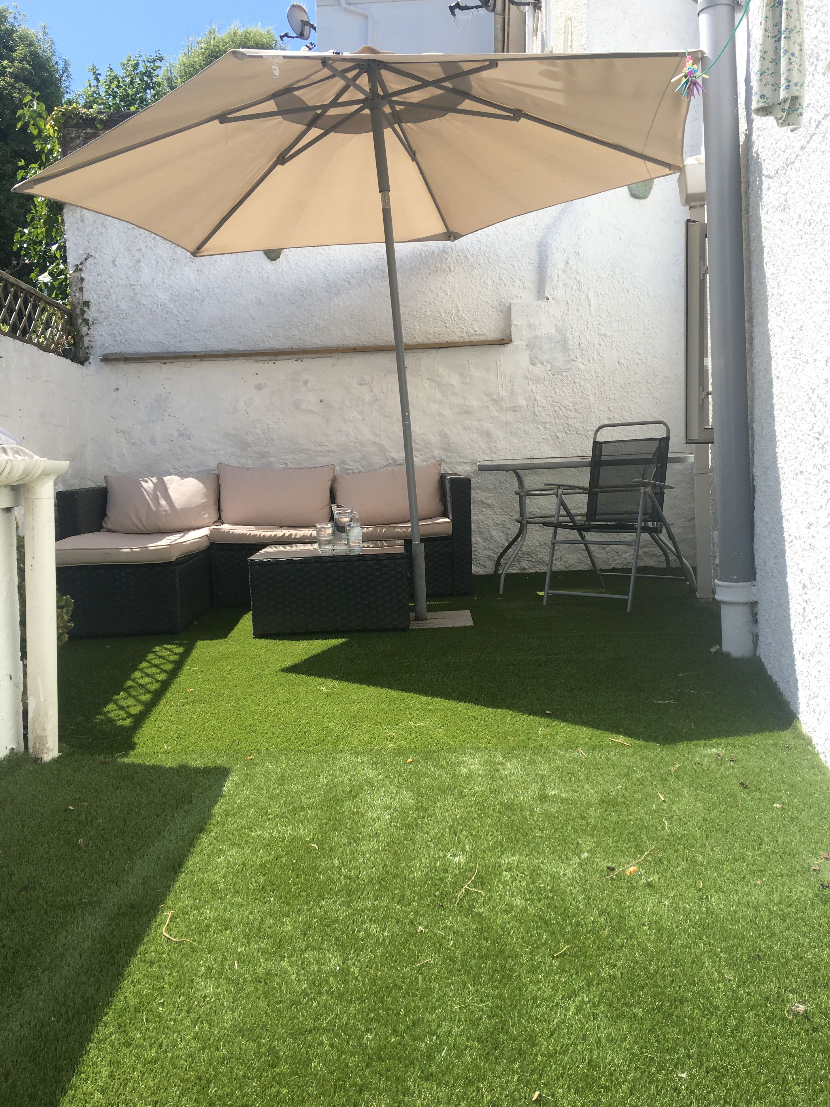 Un espace patio avec un parasol beige, un canapé et une table avec des chaises.