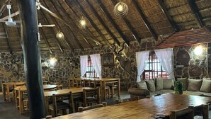 A rustic dining area with wooden tables and chairs, stone walls, and a thatched roof. - Thabankwe Bushveld Inn (Thabazimbi)
