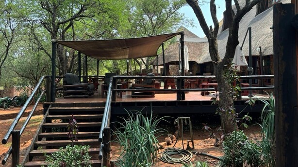 A wooden deck with outdoor seating, a covered area, and a staircase leading to a building. - Thabankwe Bushveld Inn (Thabazimbi)