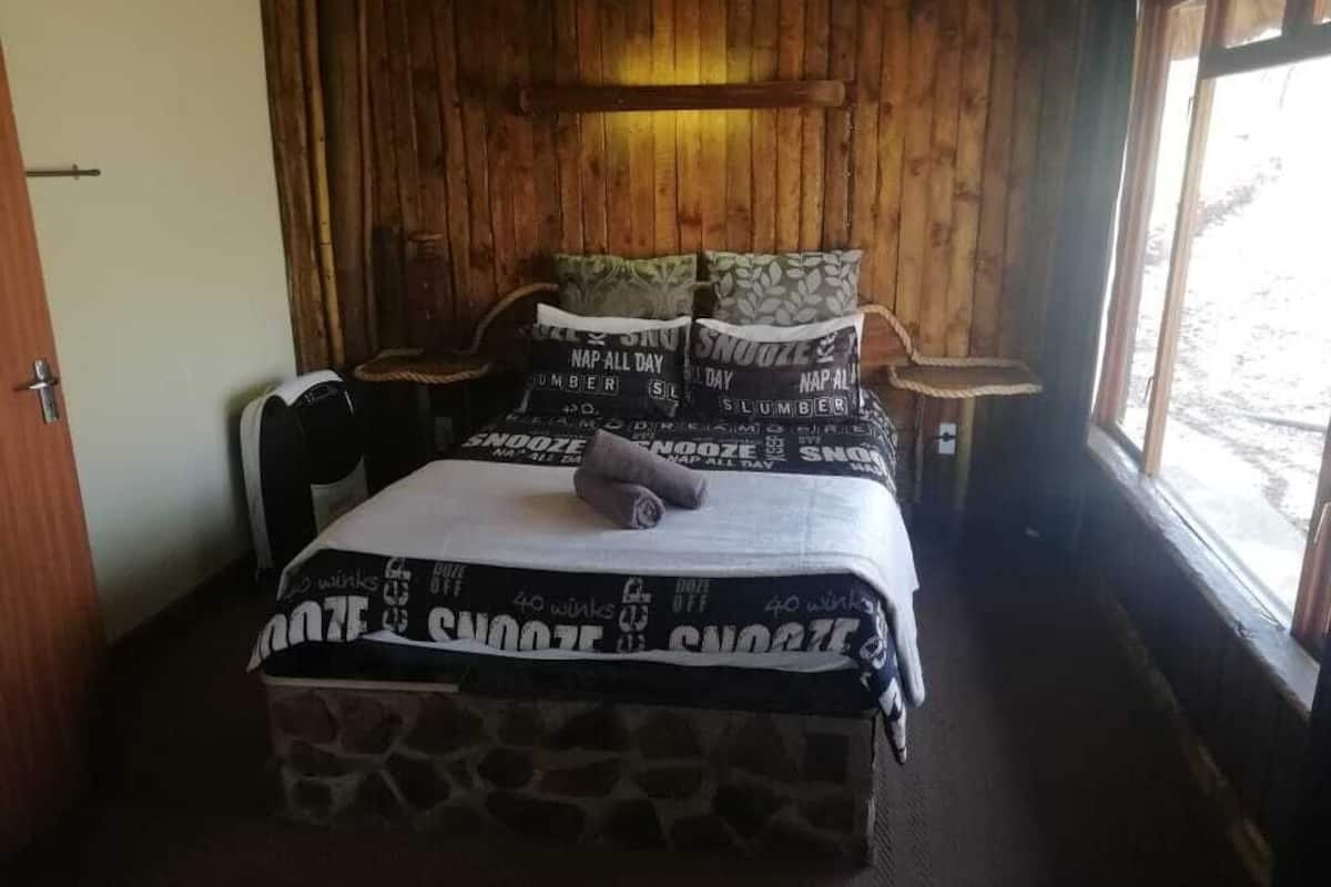 A wooden cabin-style room with a bed, pillows, and a nightstand.