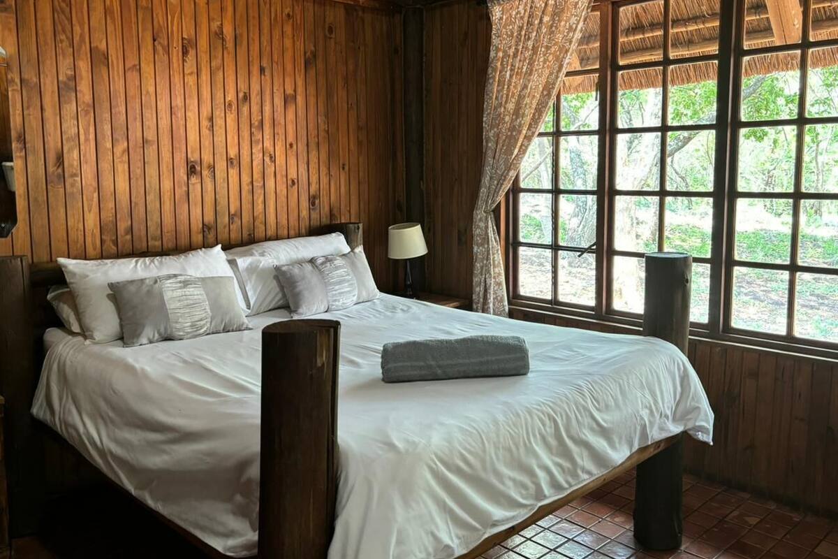 A wooden room with a bed, a window, and a lamp.