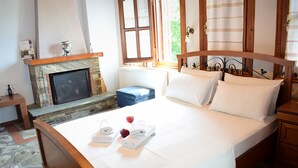 Une chambre avec une cheminée en pierre, un lit recouvert de draps blancs et une vue sur la verdure environnante.