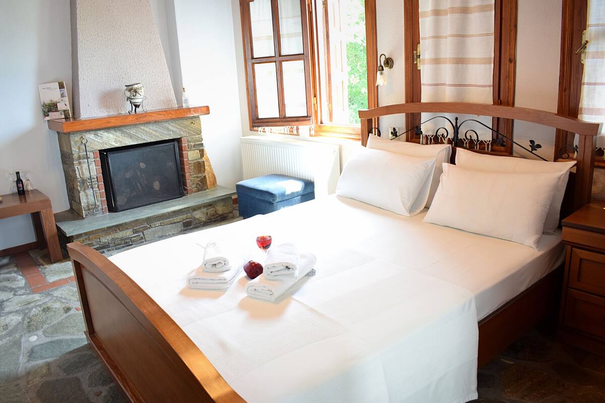 Een slaapkamer met een stenen openhaard, een bed met witte lakens en uitzicht op groen.