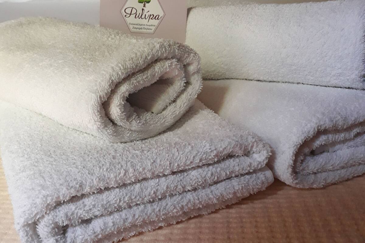 Een keurig opgevouwen witte handdoek met een label met de tekst 'Pulipa' op een getextureerd laken.