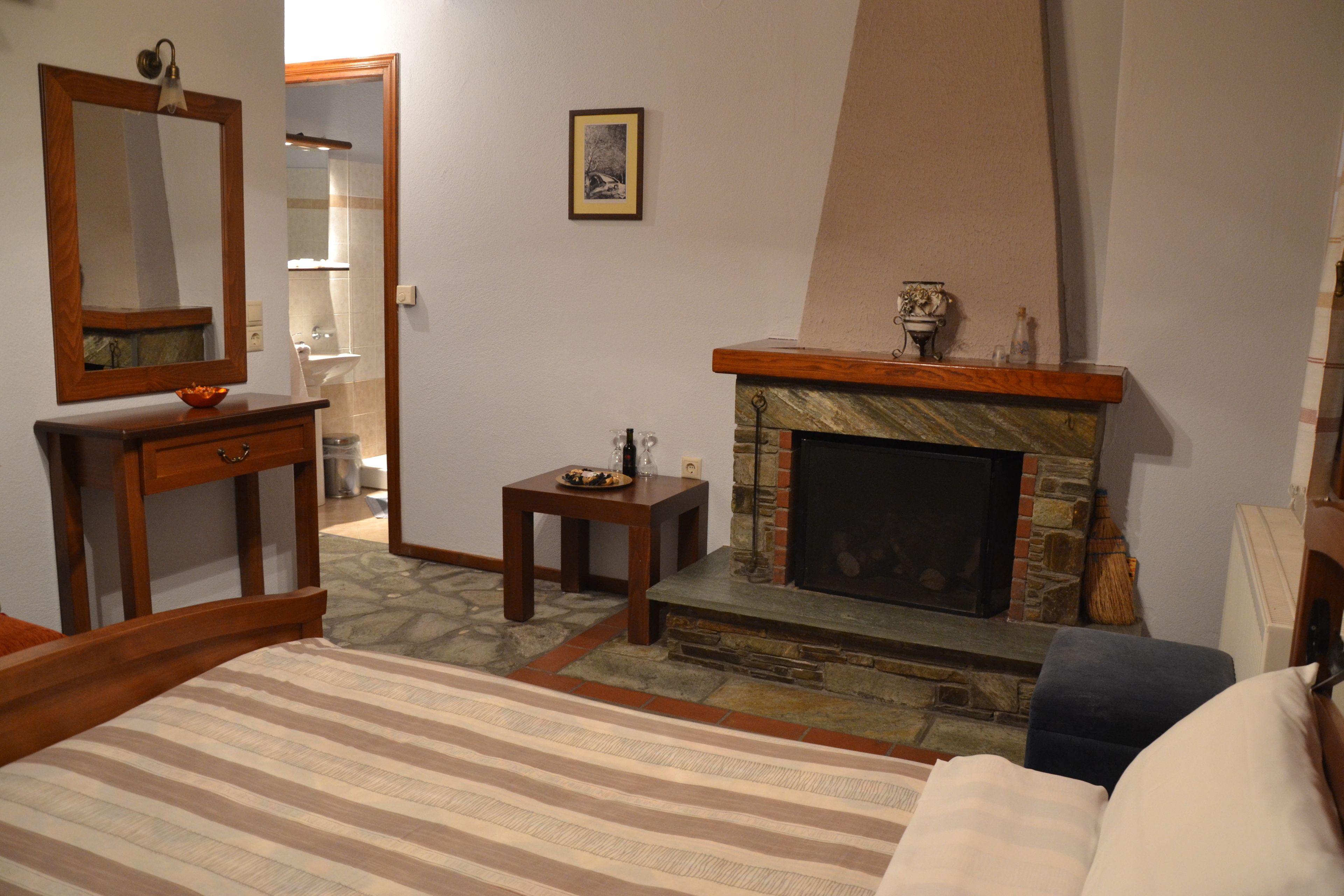 A bedroom with a bed, a dresser, a mirror, a fireplace, and a bathroom visible through an open door.