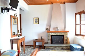 A bedroom with a stone fireplace, wooden furniture, a television, and a window. - Guesthouse FILIREA (Zagora-Mouresi)