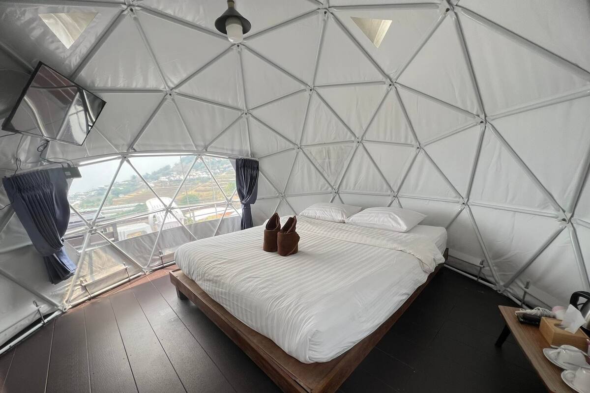 A spacious tent-style bedroom with a large bed, wooden floor, and a view of the landscape through a window.
