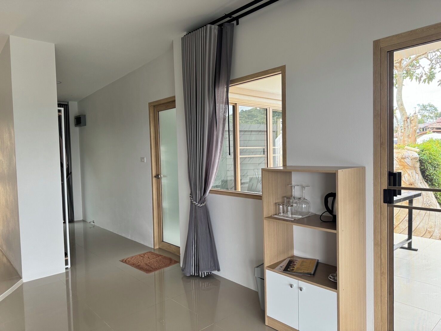 Un interior moderno con una puerta corredera, un mueble de madera con cristalería y vistas a un jardín por una ventana.