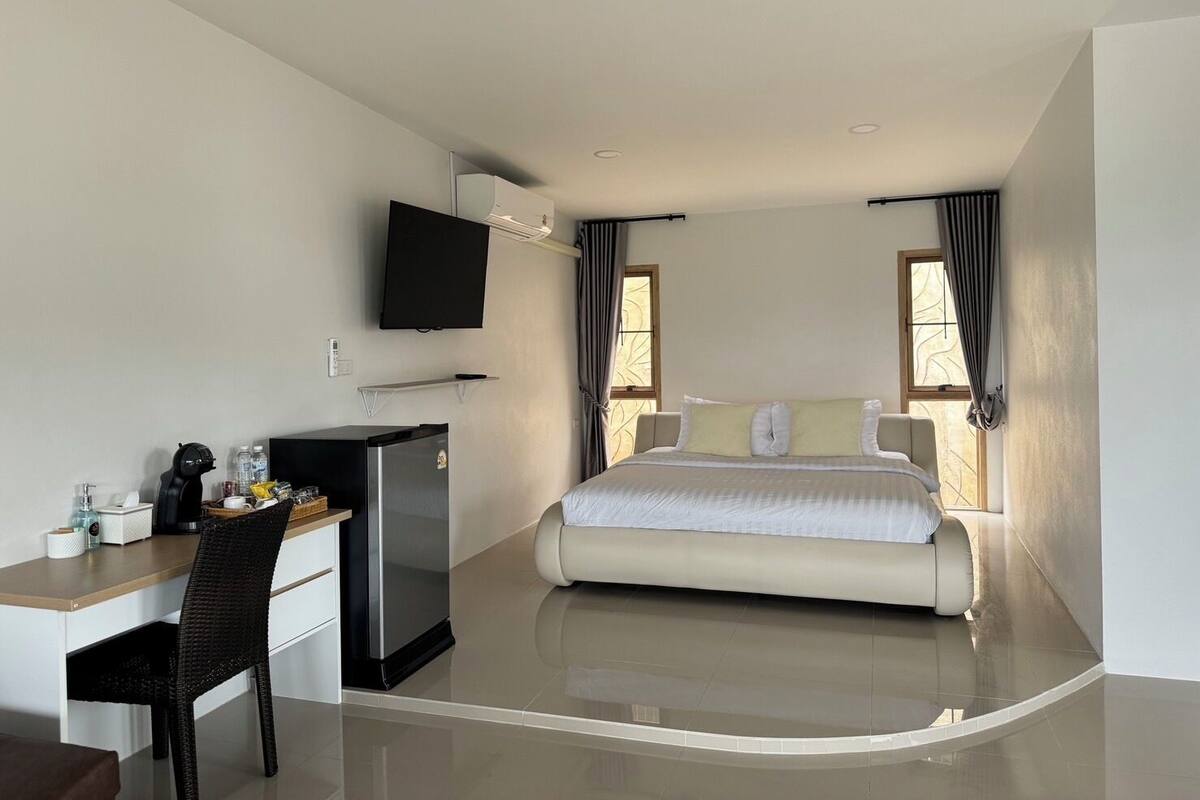 A modern hotel room with a bed, a desk, a TV, and a refrigerator.