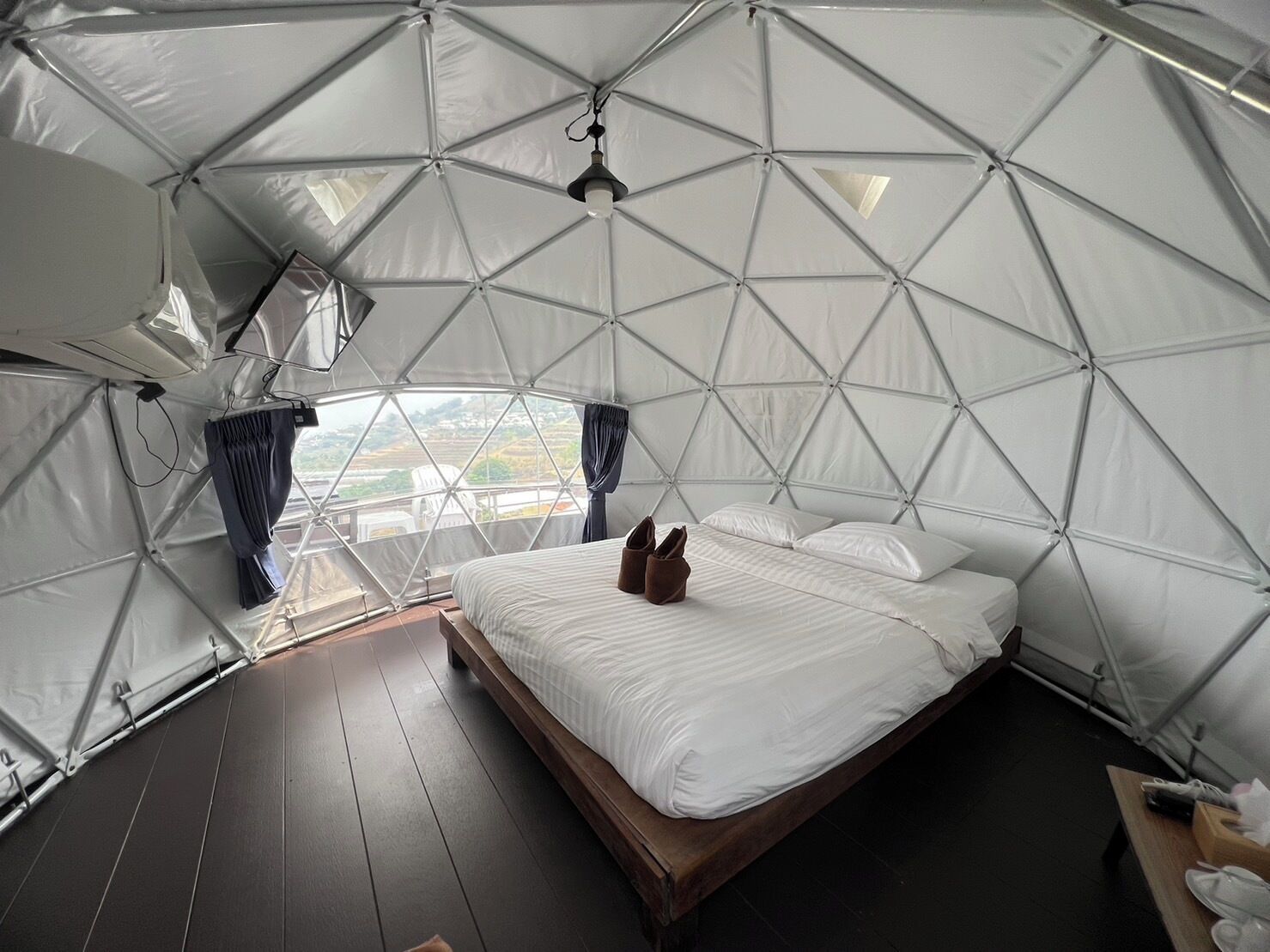A dome-shaped tent with a bed, a hanging light fixture, and a view of the landscape.