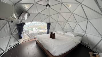 A dome-shaped tent with a bed, a hanging light fixture, and a view of the landscape.