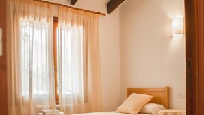 A hotel room with two beds, a window with sheer curtains, and a wooden ceiling beam. - SINGLE FAMILY HOUSE ISOLATED WITH POOL, RURAL HOUSE IN A LAND OF 35. 000M2 (Selva- Cami Selva- Mallorca)
