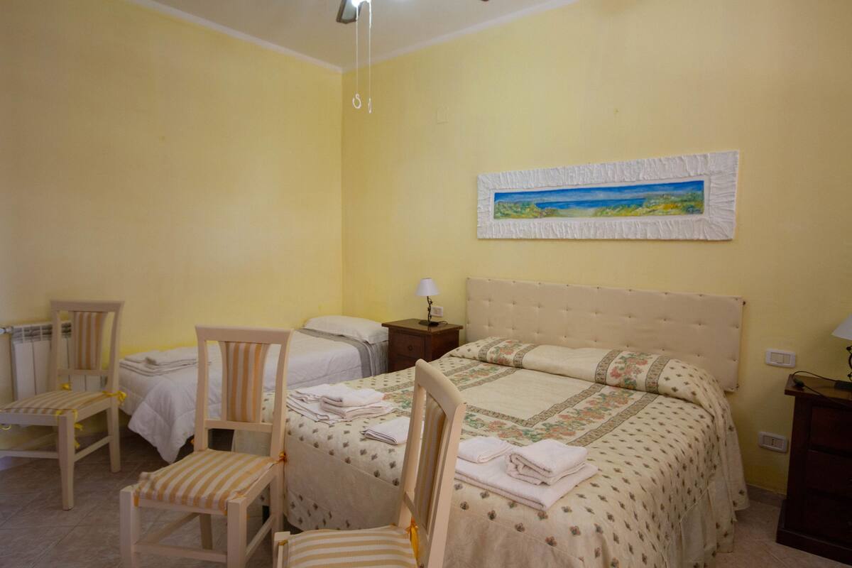A bedroom with two single beds, a chair, a nightstand, and a painting on the wall.