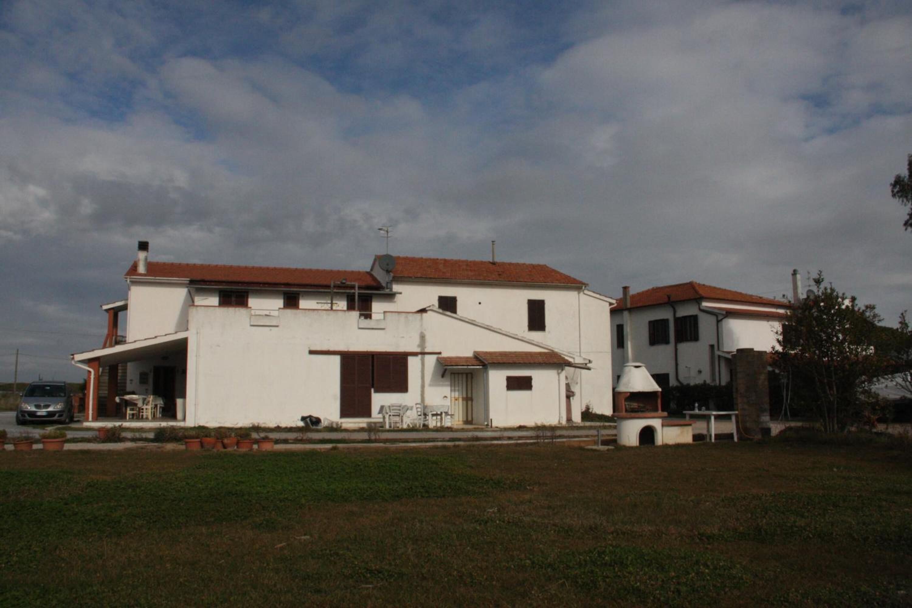 Una casa blanca de dos pisos con techo de tejas rojas, un patio con mobiliario exterior y una pequeña cocina al aire libre.