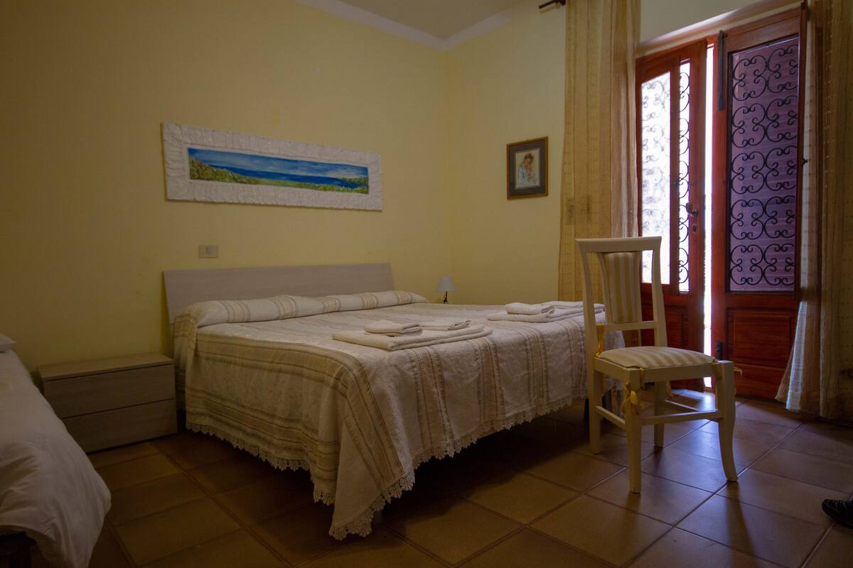 A bedroom with a bed, a chair, a painting, and a door with a patterned design.