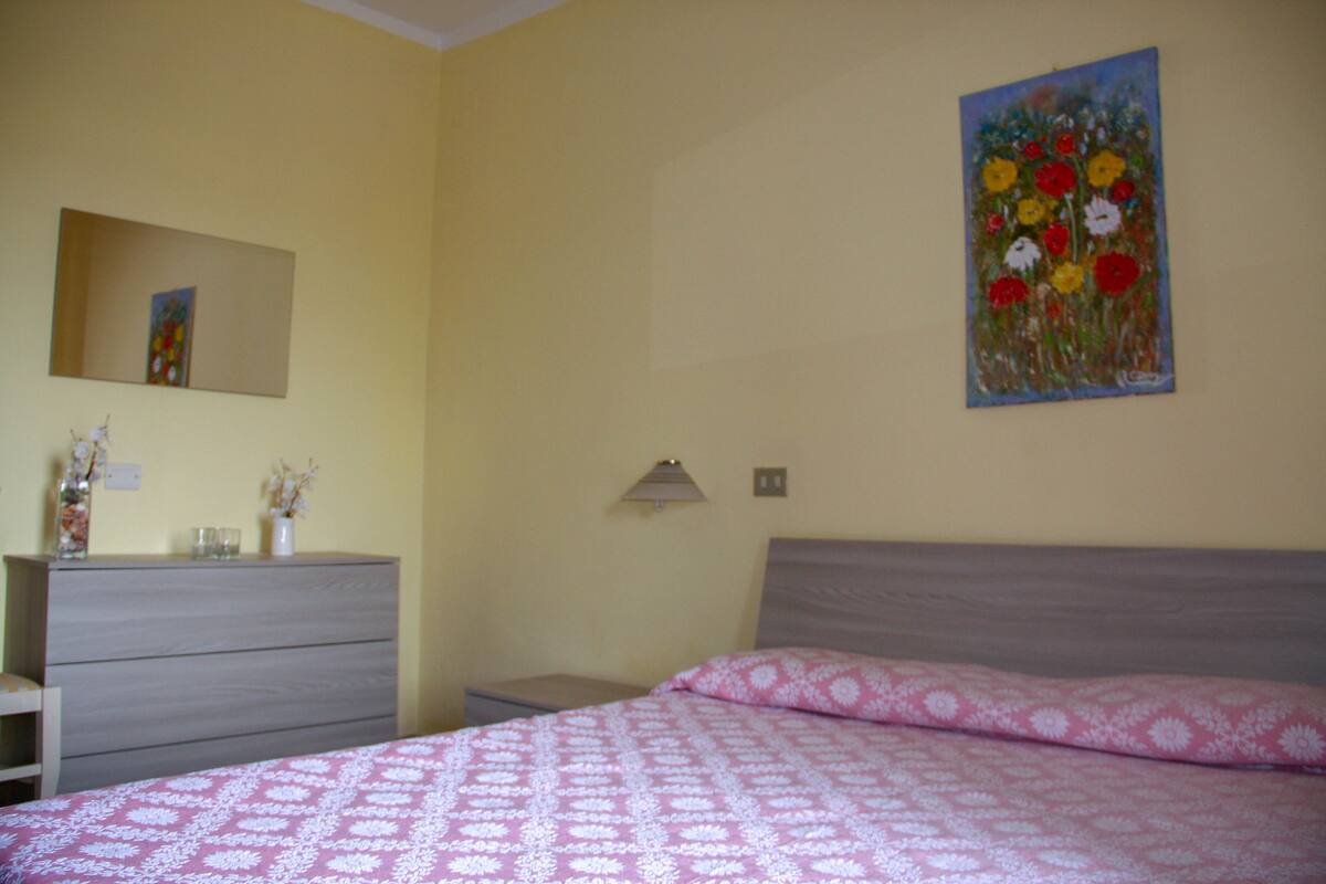 A bedroom with a bed, dresser, nightstand, and a painting on the wall.